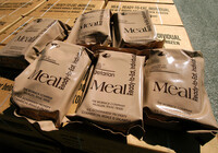 Meals Ready to Eat (MREs) in beige bags are displayed on top of a pallet of cases in position to be placed into vehicles.